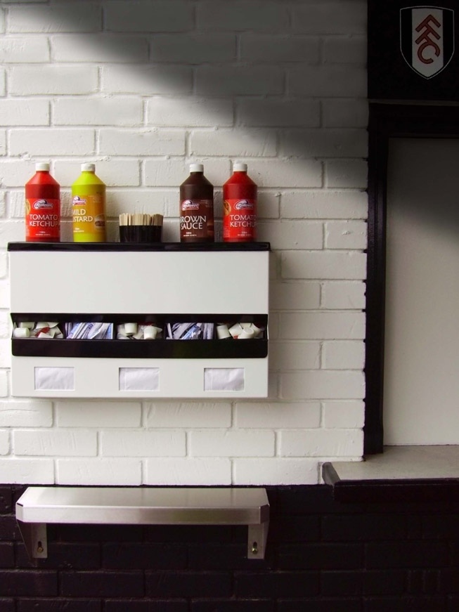 Sauce Station at Fulham F.C's Stadium showing sauce bottle holder middle acrylic sachet dispenser in ABS plastic, and Napkin dispensers. An early Stainless Steel Saucing shelf sits below .